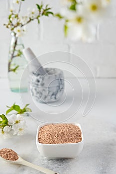 Ceramic bowl with red clay powder, ingredients for homemade facial and body mask or scrub and fresh sprig of flowering cherry