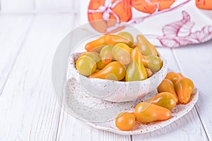 Ceramic bowl with yellow pear tomatoes on white wooden background. Free space