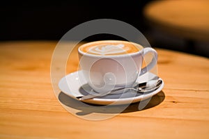 Ceramic cup in coffee shop with cappuccino on wooden empty table. Latte art. Morning drink. Caffeine.
