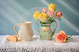 ceramic cup, creamer, and pastel roses on lace cloth