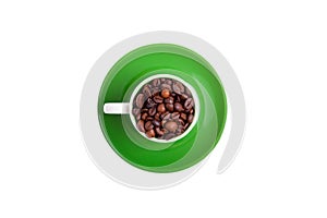 Ceramic cup on a green saucer filled with coffee beans, top view