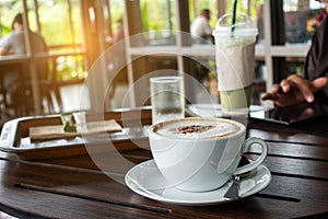 The ceramic cup of hot cappuccino coffee on the wooden table in the restaurant or coffee shop. natural light. morning hot drink