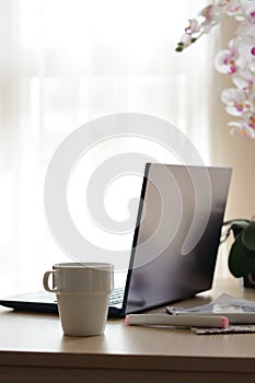 Ceramic cup, laptop and stationery on wooden table indoors. Good morning