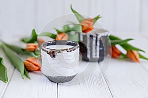 Ceramic cup with milk and spring orange tulips on a white wooden background. Free space