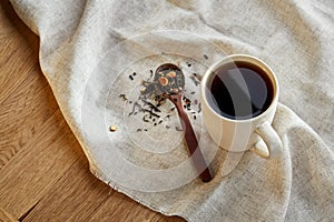 Ceramic cup of tea with scattered tea leaves on a napkin on rustic wooden background, selective focus