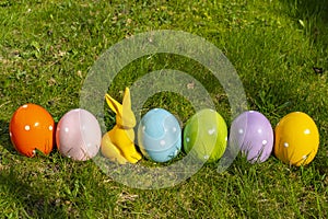 Ceramic easter eggs and an Easter bunny in a line on a meadow
