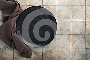 Ceramic empty black plate and linen kitchen towel napkin on old ceramic tile table background. Cooking stone backdrop. Top view