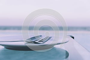 Ceramic empty dish with fork and spoon on the glass table. It is setting for dinner on the beach.