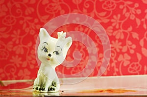 Ceramic figurine cute white cat on red background.