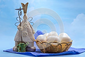 Ceramic figurine of an Easter bunny next to white, unpainted eggs in a wicker basket against the sky. Free space. Easter