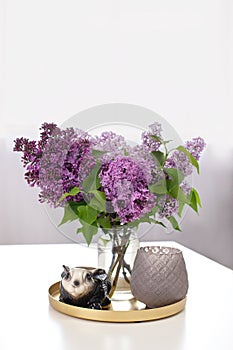 Ceramic figurine of rabbit bunny next to bouquet of lilac flowers in vase and candlestick on an table, on an isolated white backgr
