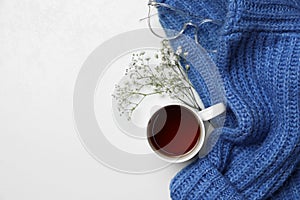 Ceramic mug with aromatic tea, blue knitted sweater, glasses and beautiful dry flowers on white background, flat lay. Space for