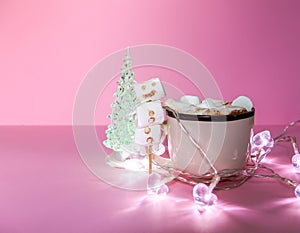 Ceramic mug with hot fresh cocoa drink and handmade funny marshmallow snowman on soft pink background