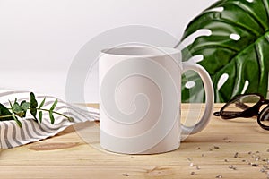 Ceramic mug on wooden desktop next to striped tablecloth, scattered crystals and green plants on white background. Close