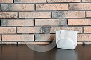 Ceramic napkin holder with paper serviettes on table near brick wall.