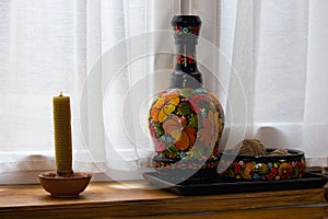 Ceramic painted vase and pot and candle on windowsill. Traditional ukrainian handmade decoration. Ethnic rustic souvenirs.