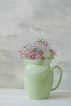 ceramic pale light green jug with small colorful gypsophila flowers on a light background.