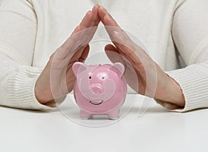 A ceramic piggy bank and female hands above it, a concept of saving money