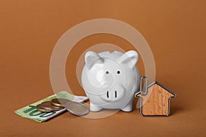 Ceramic piggy bank, money and key trinket on brown background. Financial savings
