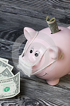 Ceramic piggy bank in pink. With a gauze bandage. In front of her are a few dollar bills. One of them sticks out of the slot.