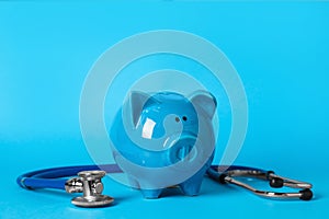 Ceramic piggy bank and stethoscope on light blue background. Medical insurance