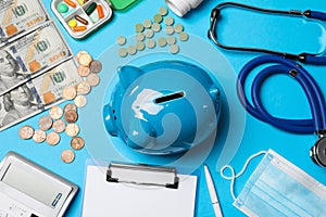 Ceramic piggy bank, stethoscope, money and pills on light blue background, flat lay. Medical insurance