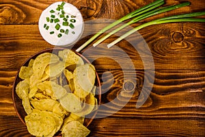 Ceramic plate with potato chips and glass bowl with sour cream on wooden table. Top view