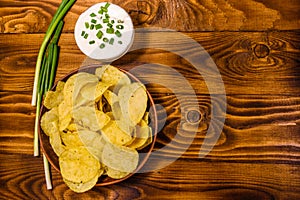 Ceramic plate with potato chips and glass bowl with sour cream on wooden table. Top view