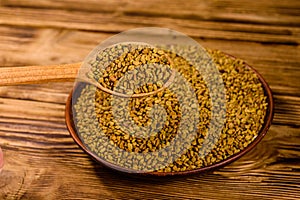 Ceramic plate and spoon with fenugreek seeds on wooden table