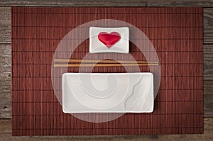 A ceramic plate for sushi and japanese food with chopstick and bowl for soy sauce with a heart inside top view