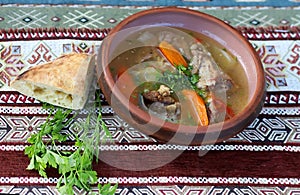 Ceramic plate of traditional Armin soup with meat, carrots and herbs and bread on a beautiful tablecloth background photo