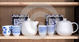 Ceramic teapots and cups with blue ornaments on a wooden kitchen shelf