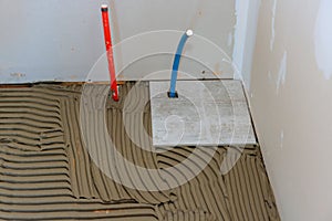 Ceramic tile is being placed over adhesive on a bathroom floor by tiler