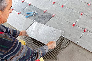 Ceramic Tiles. Tiler placing ceramic wall tile in position over adhesive with lash tile leveling system