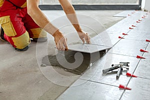 Ceramic Tiles. Tiler placing ceramic wall tile in position over adhesive with lash tile leveling system photo