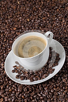 Ceramic white cup of coffee cream with roasted beans on grains background