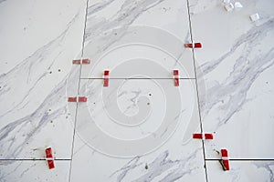 Ceramic white floor tiles laid over adhesive with a tile leveling system