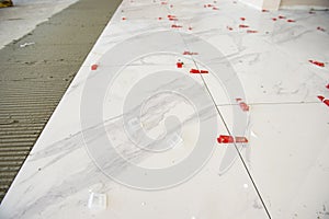 Ceramic white floor tiles laid over adhesive with a tile leveling system