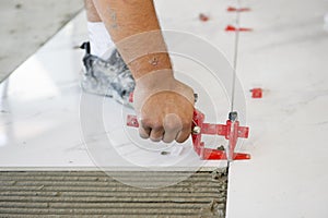 Ceramic white floor tiles laid over adhesive with a tile leveling system