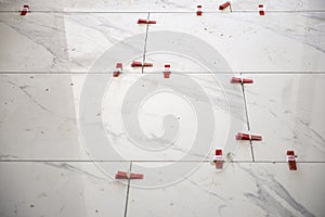 Ceramic white floor tiles laid over adhesive with a tile leveling system