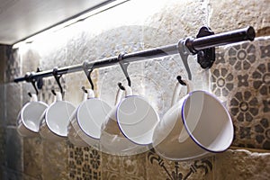 Ceramic white mugs hanging on hooks in the kitchen