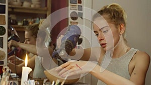 A ceramicist girl dries a clay product with a hair dryer in the workshop.