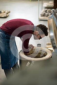 Ceramist Dressed in an Apron Placing Clay Sculpture in Electric Oven.