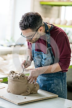 Ceramist Dressed in an Apron Sculpting Statue from Raw Clay in Bright Ceramic Workshop. photo