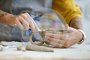 Ceramist hands shaping ceramic cup of raw clay material using professional potter tools in workshop