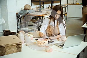 Ceramist with laptop working in studio, making notes