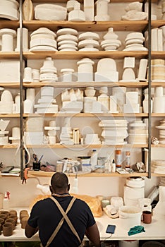 Ceramist working at a bench under shelves full of pottery molds