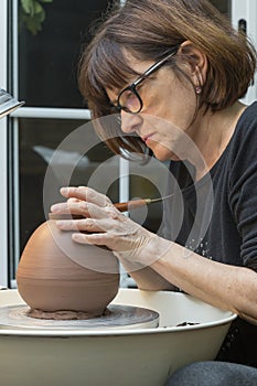 ceramist working on the lathe with a piece to which he is chipping away with a tool