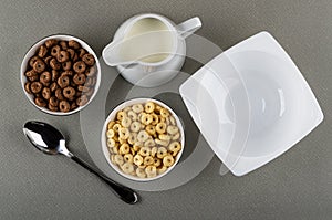 Cereal breakfasts with chocolate and caramel in bowls, pitcher with yogurt, spoon, empty bowl on table. Top view