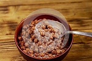 Cereal chocolate balls with milk in a bowl on wooden table. Spoon with breakfast